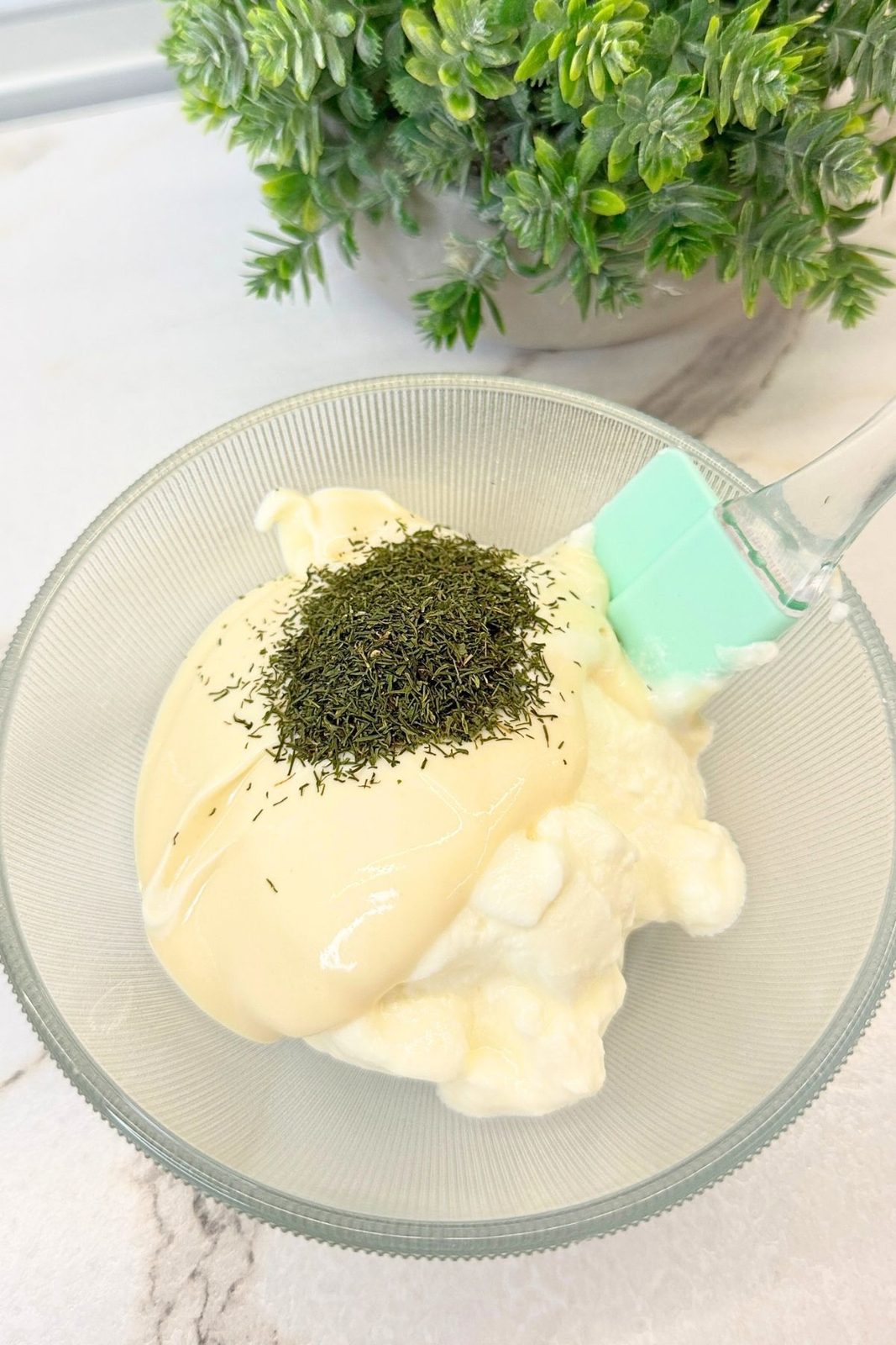 Sour cream, mayonnaise, and dried dill in a glass bowl, ready to mix into a creamy sauce.
