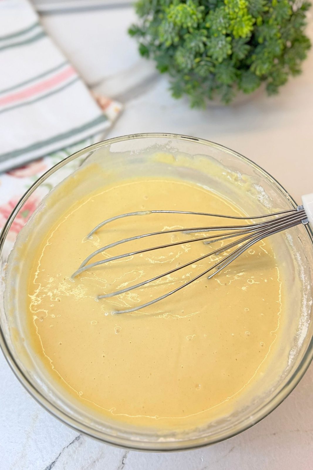 Smooth crepe batter being whisked in a glass mixing bowl until free of lumps