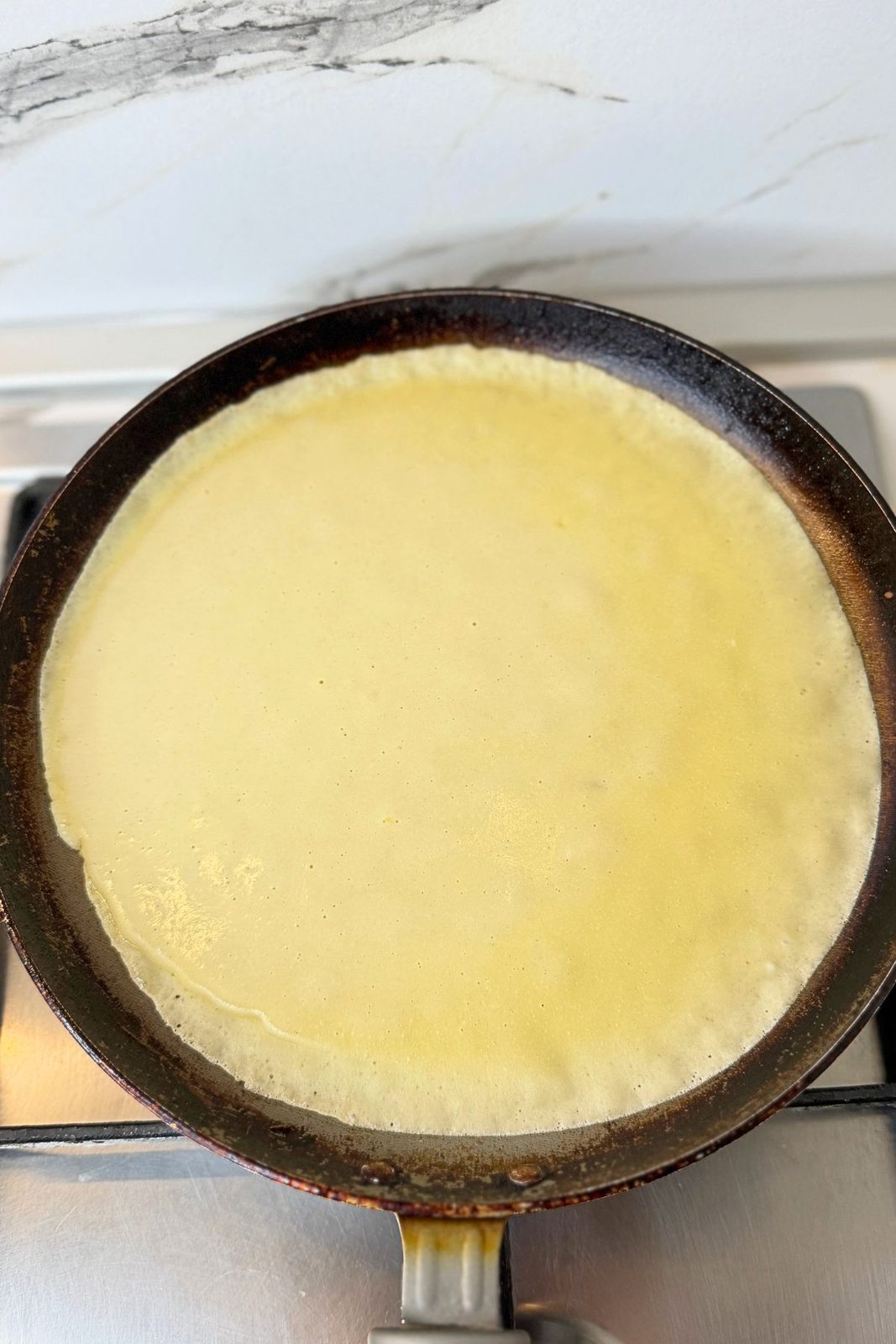 Thin crepe batter spread evenly across a hot crepe pan