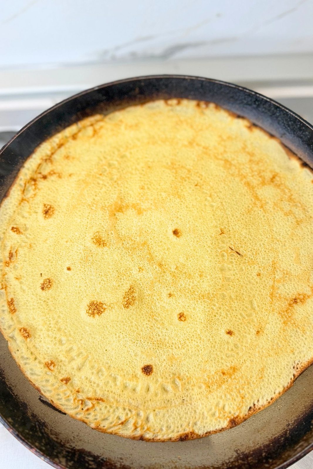 Thin homemade crepe cooking until lightly golden in a skillet
