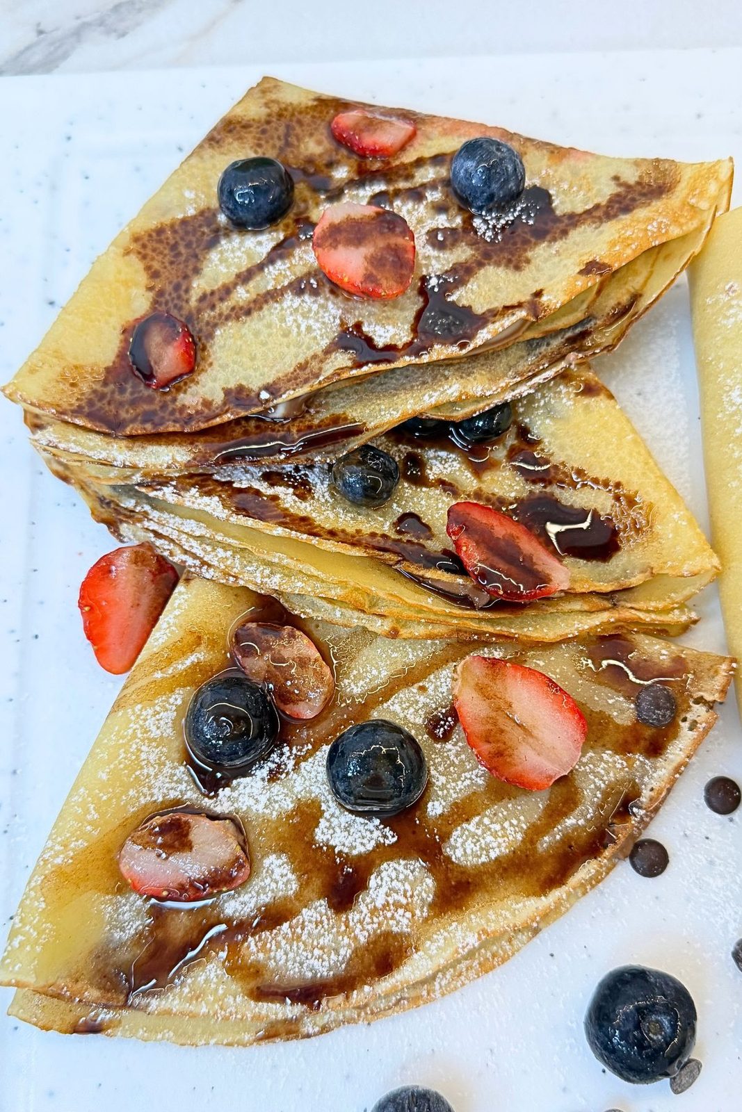 Thin homemade crepes folded into triangles and topped with Nutella, strawberries, blueberries, and powdered sugar