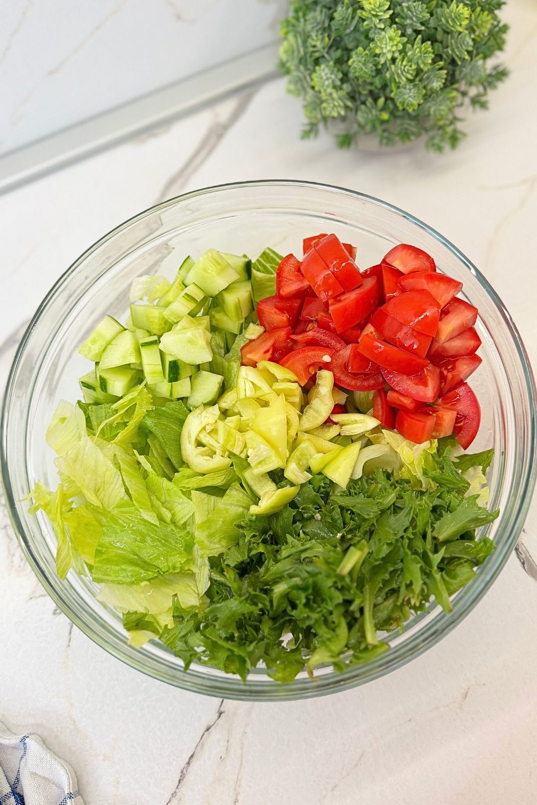 Chopped iceberg lettuce, arugula, cucumber, tomatoes, and bell pepper in a large glass bowl.