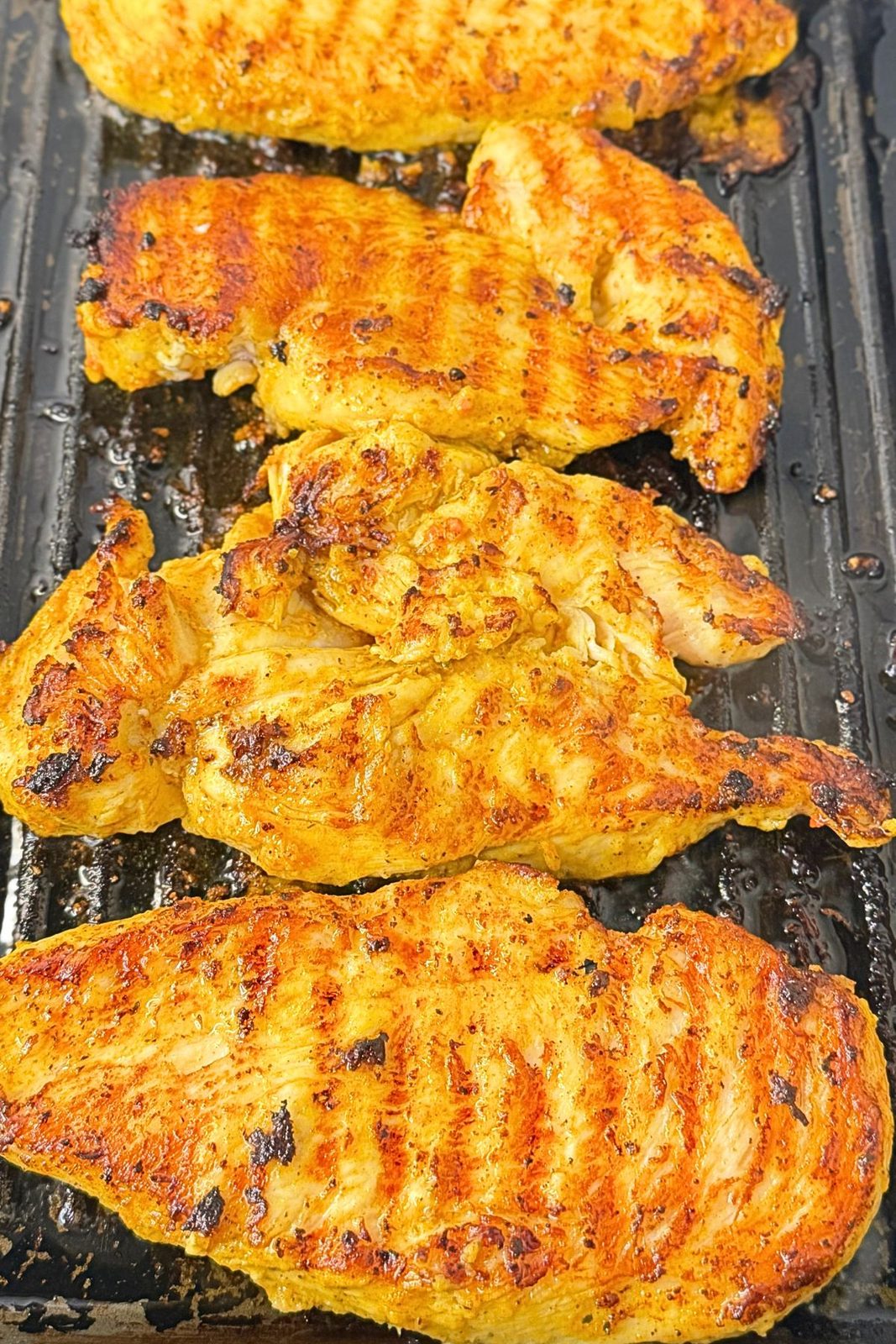 Golden grilled chicken breast cutlets cooked evenly on both sides in a grill pan.