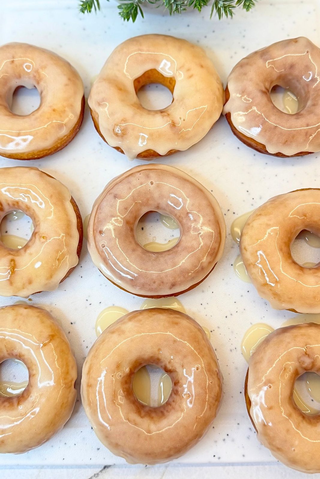 Freshly glazed donuts arranged on a white board with vanilla glaze dripping down the sides.