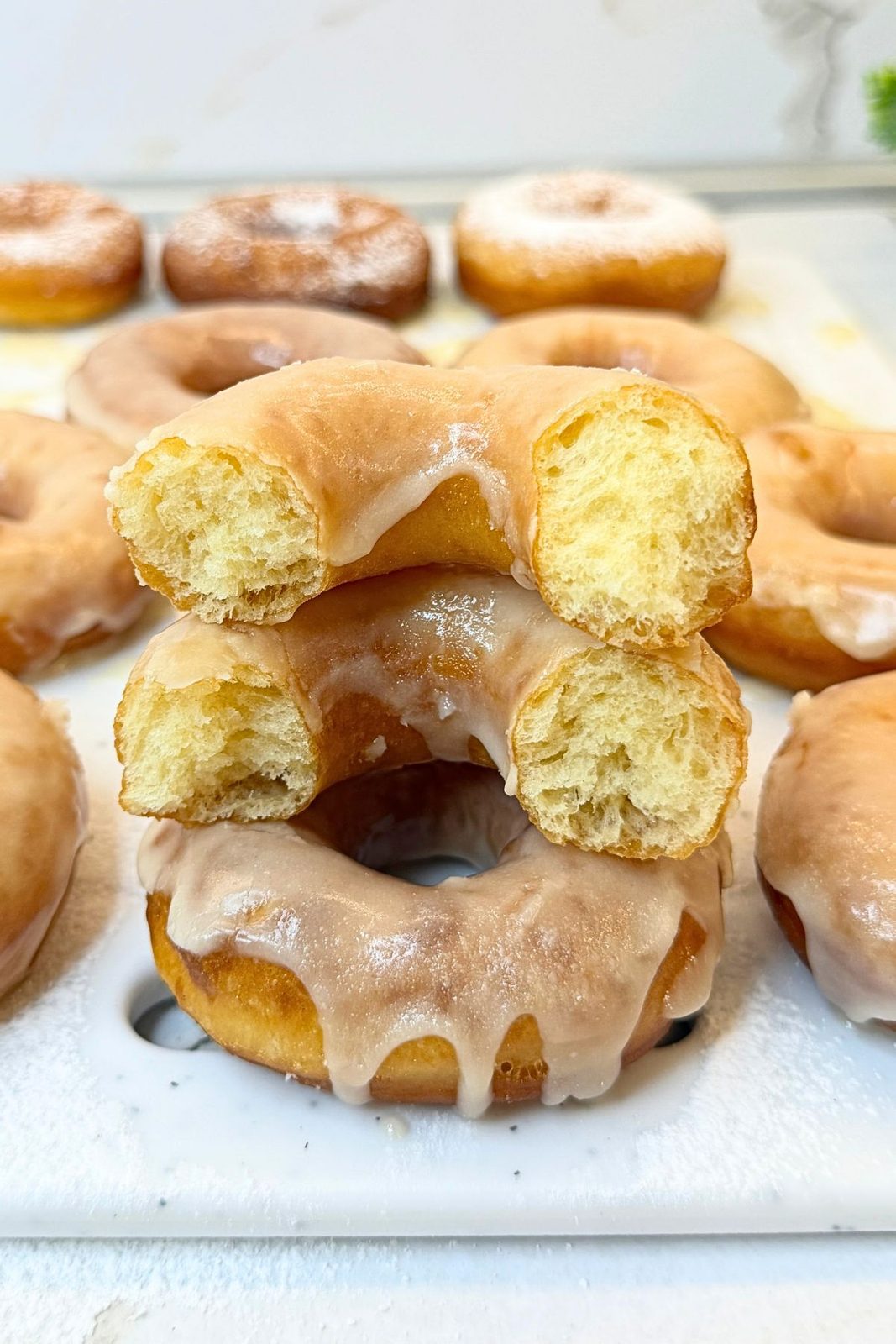 Stacked glazed donuts with cut halves showing their fluffy interior and vanilla glaze dripping down the sides.