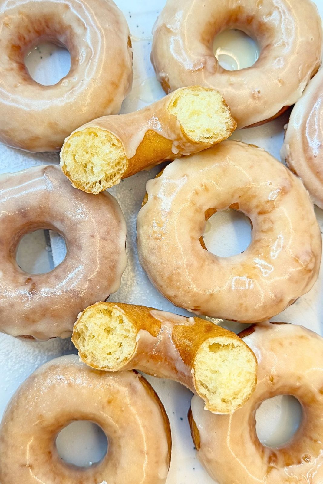 Freshly glazed donuts arranged on a white board with vanilla glaze dripping down the sides.