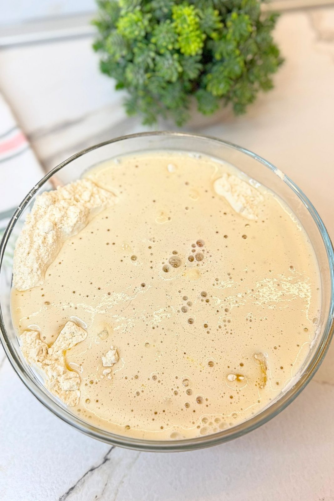 Wet ingredients added to flour in a glass bowl to make glazed donut dough.