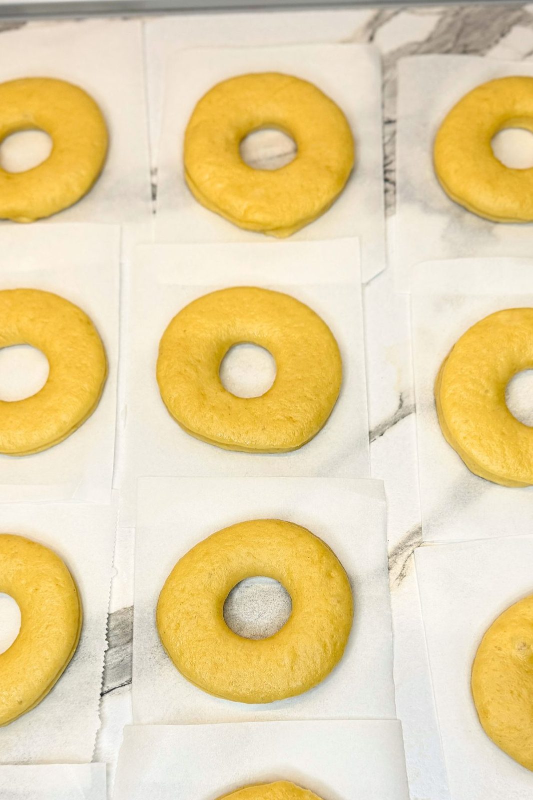 Uncooked donut rings resting on individual parchment paper squares before frying.