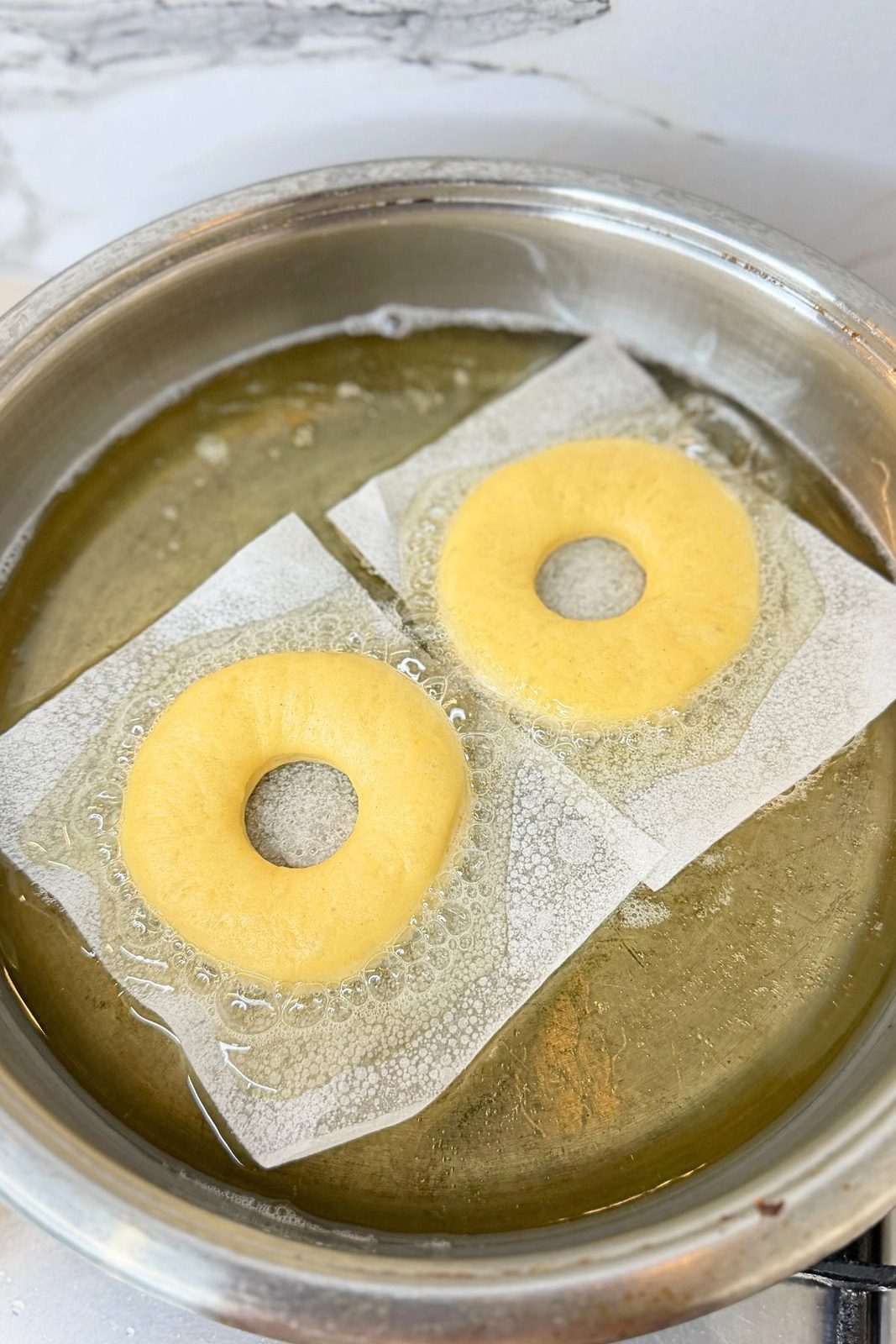 Donut rings on parchment paper squares being lowered into hot oil for frying.