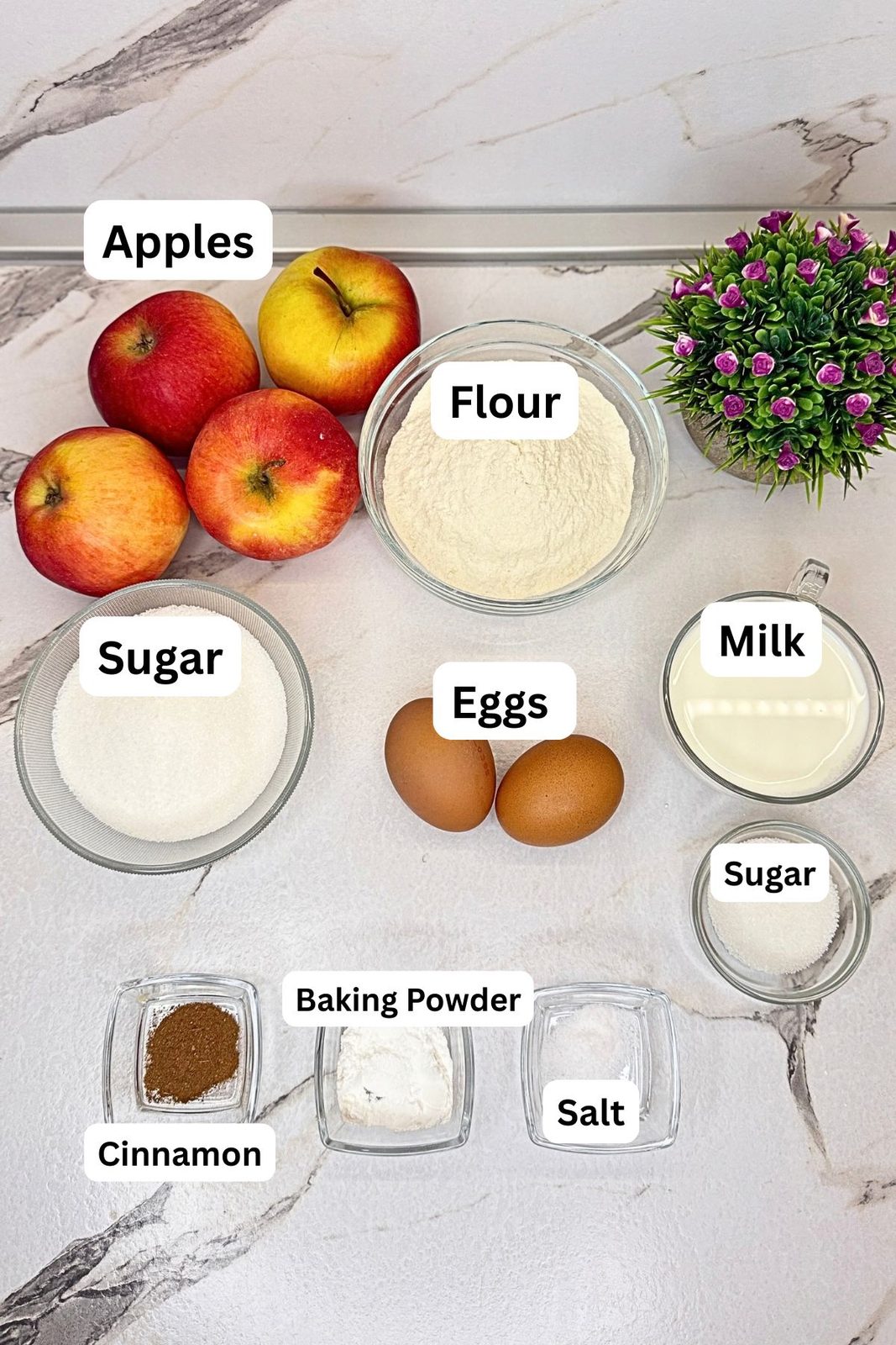Ingredients for homemade apple fritters, including apples, flour, sugar, milk, eggs, baking powder, salt, and cinnamon, arranged in labeled bowls.
