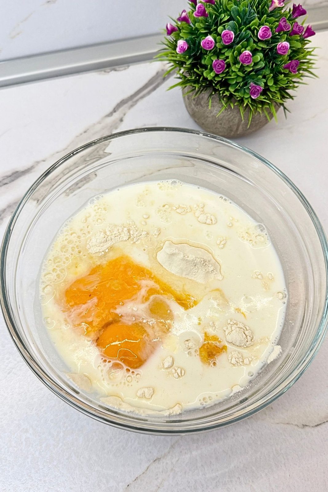 Flour, milk, and eggs in a glass bowl before mixing the homemade apple fritter batter.