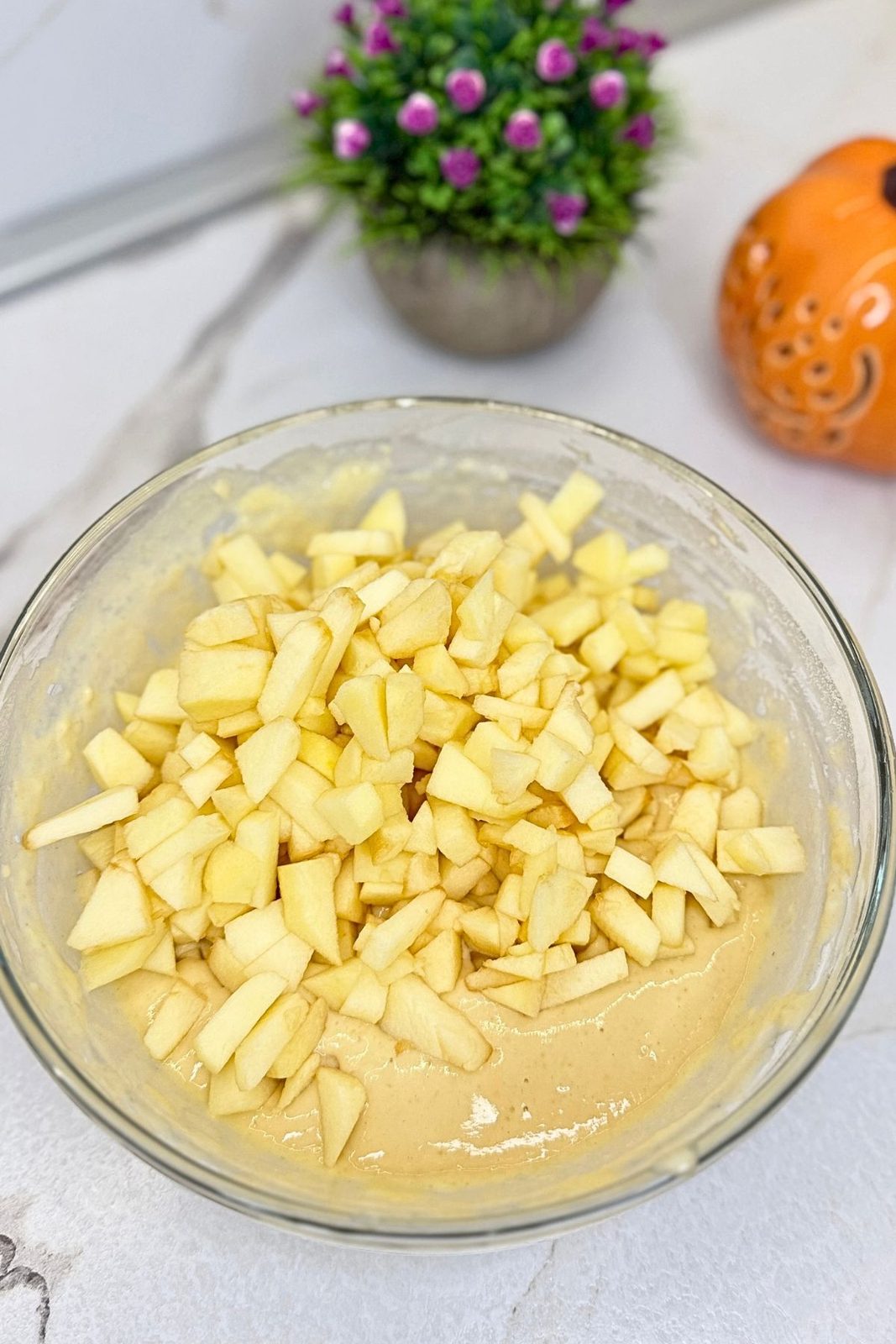 Peeled and chopped apples added to apple fritter batter in a glass mixing bowl.