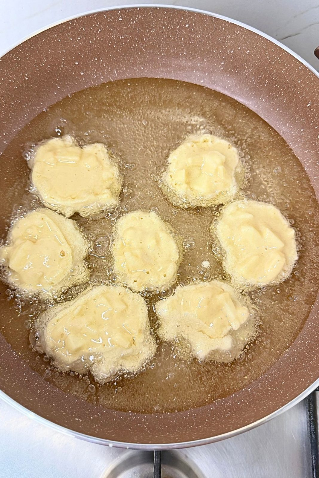 Small portions of homemade apple fritter batter frying in bubbling oil in a deep skillet.