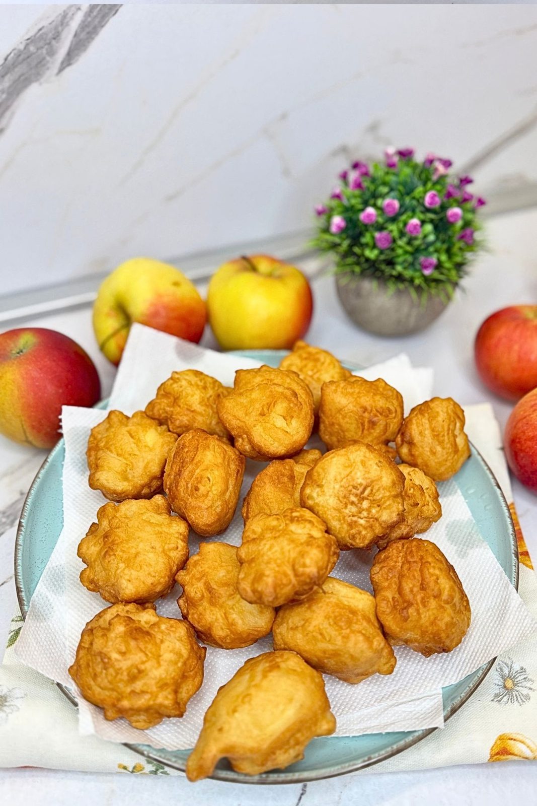 Golden homemade apple fritters draining on a paper towel-lined blue plate.