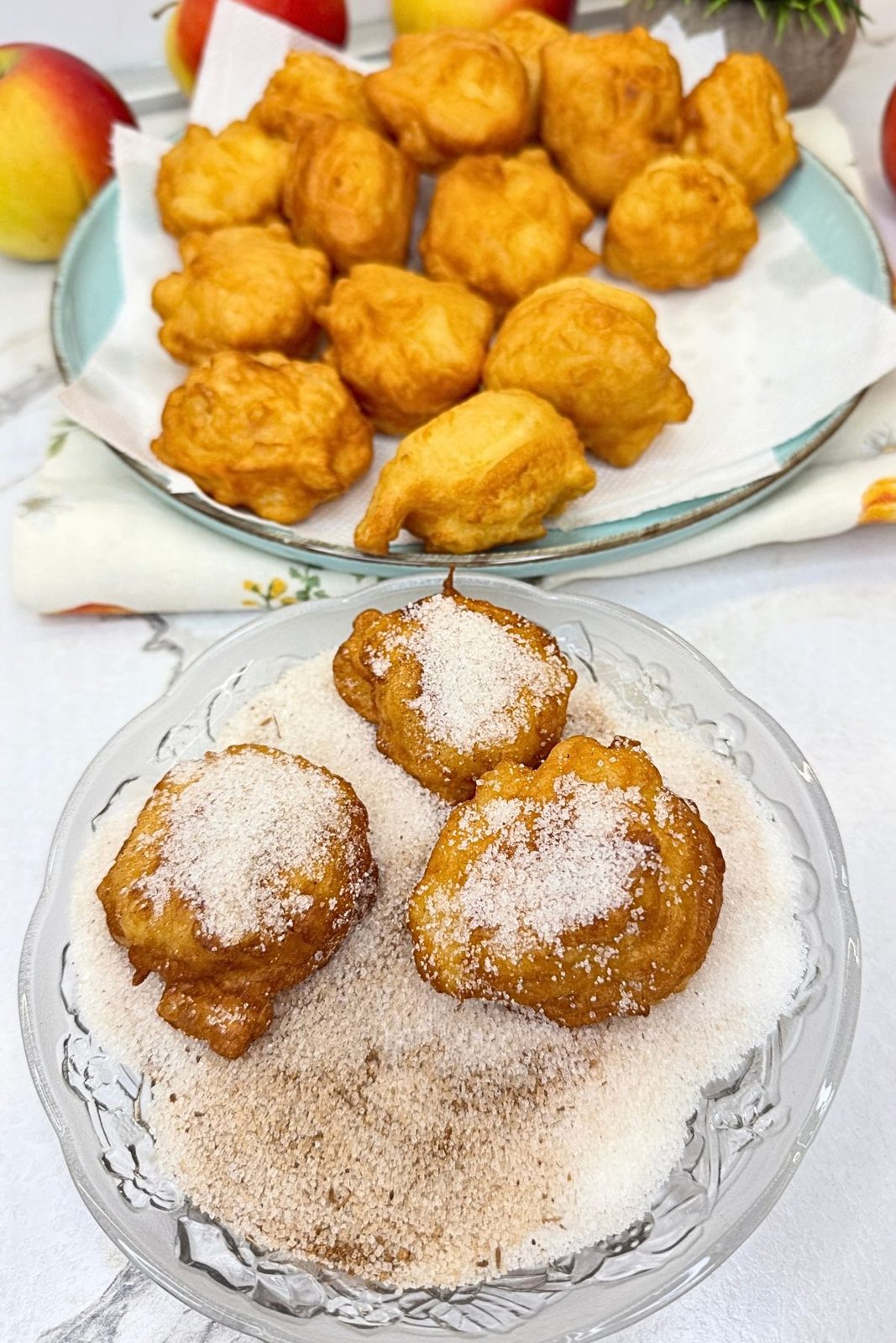 Freshly fried apple fritters being coated in cinnamon sugar on a glass plate.