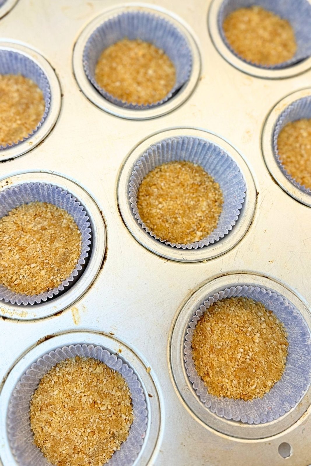 Graham cracker crust pressed into paper liners in a muffin pan