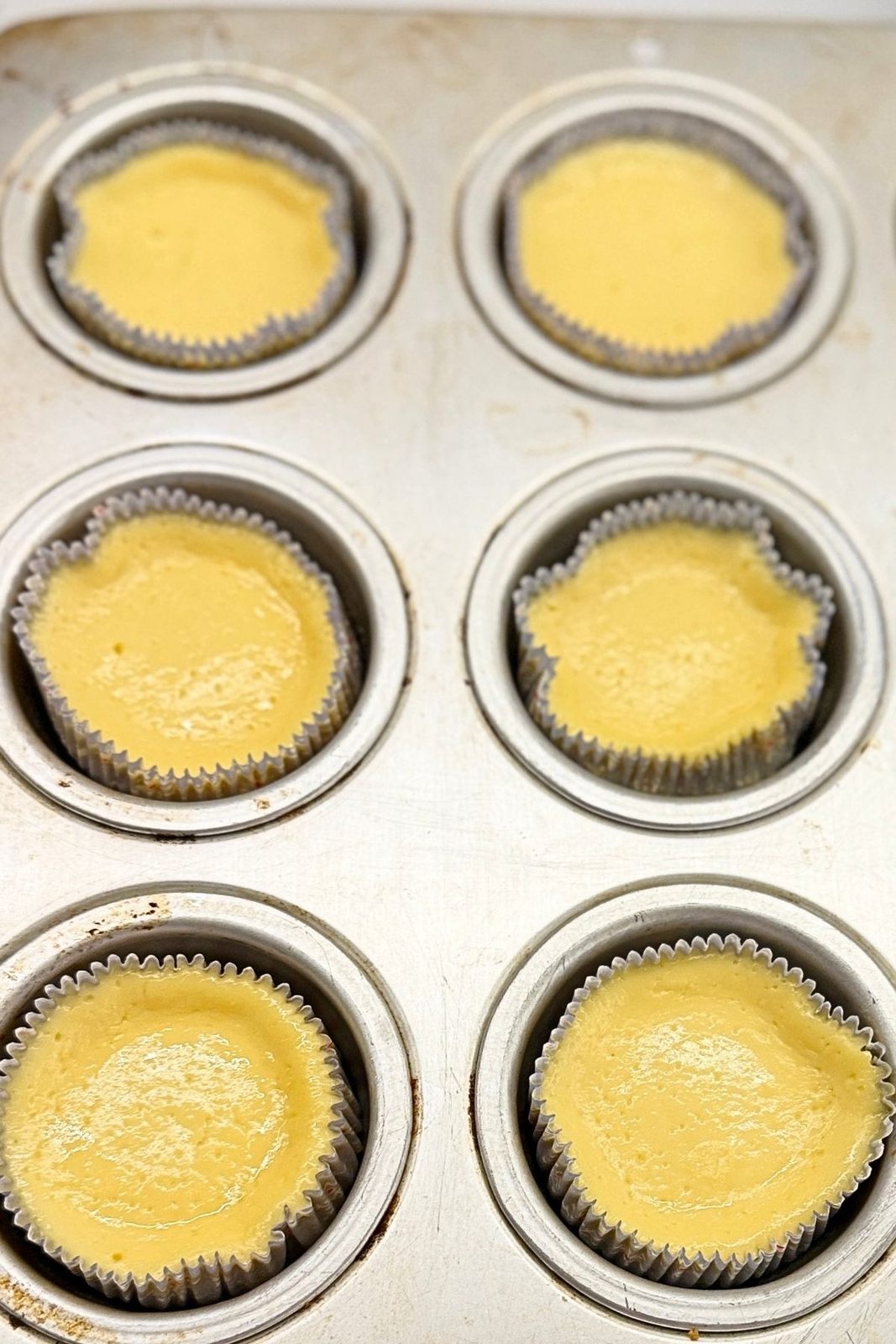 Muffin liners filled with smooth mini cheesecake batter before baking