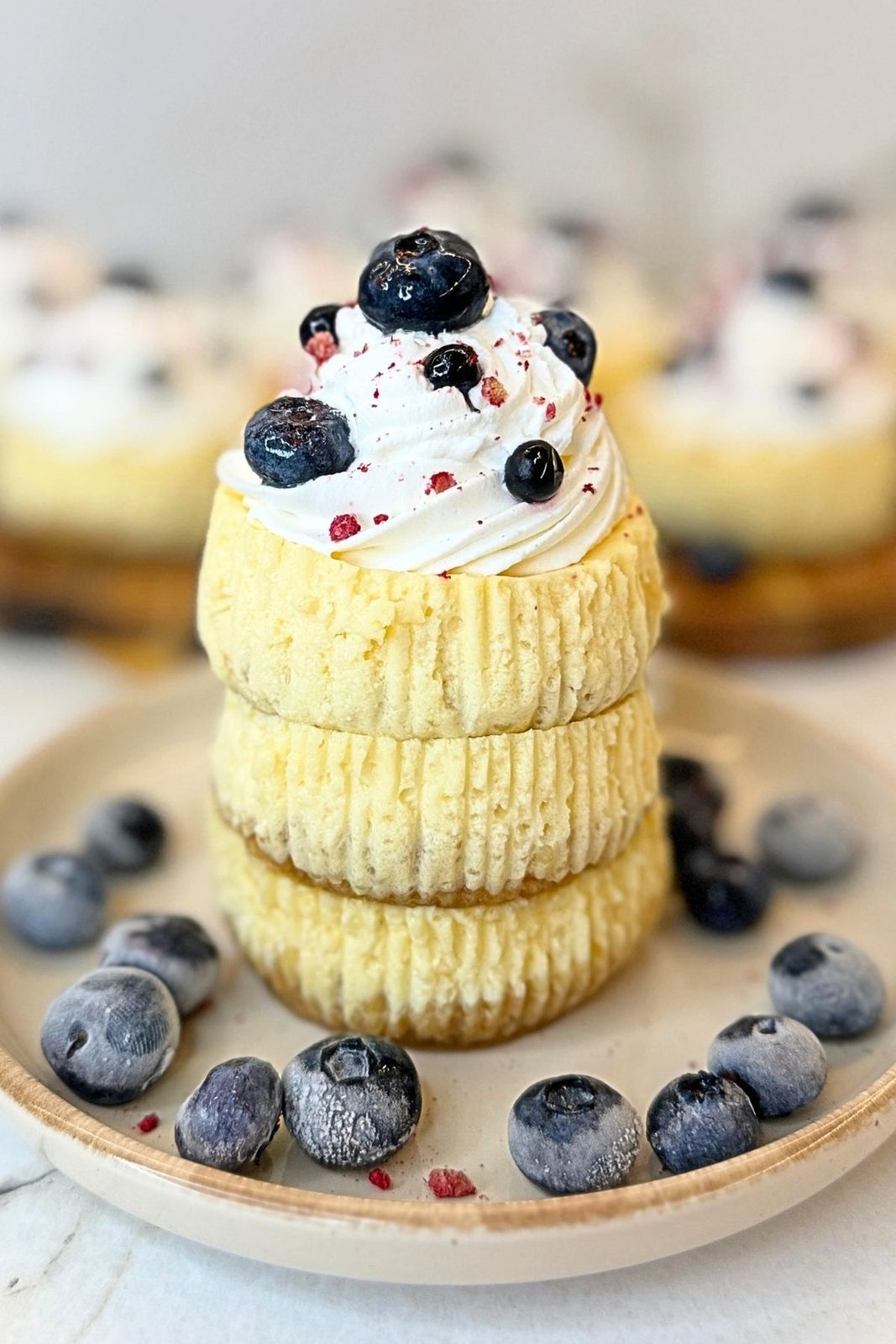 Three stacked mini cheesecakes topped with whipped cream and fresh blueberries
