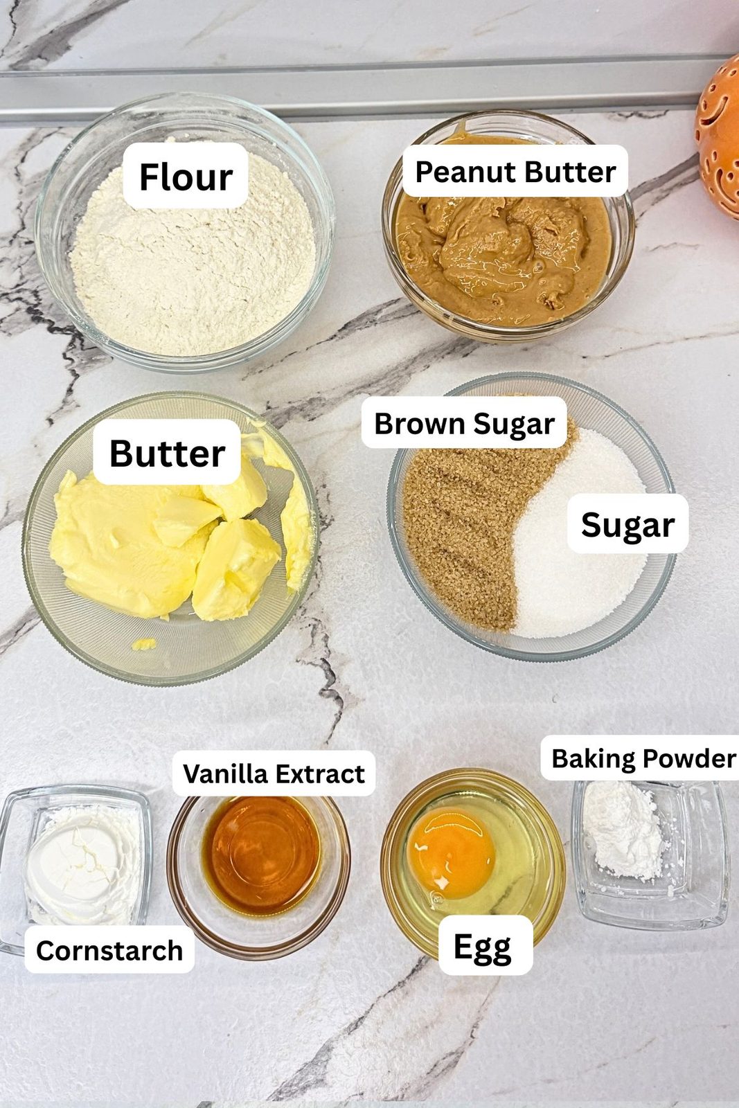 Peanut butter cookies ingredients in labeled bowls, including flour, peanut butter, butter, brown sugar, granulated sugar, vanilla extract, egg, baking powder, and cornstarch.