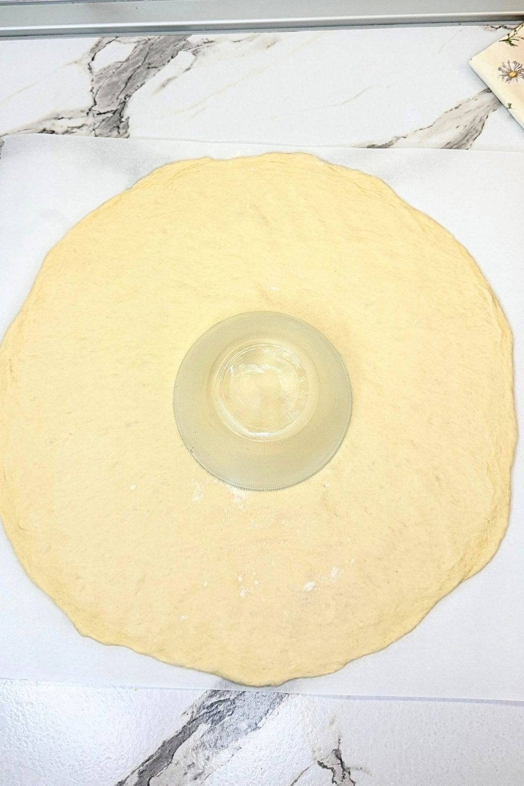Pizza dough rolled into a large circle with an upside-down bowl in the center