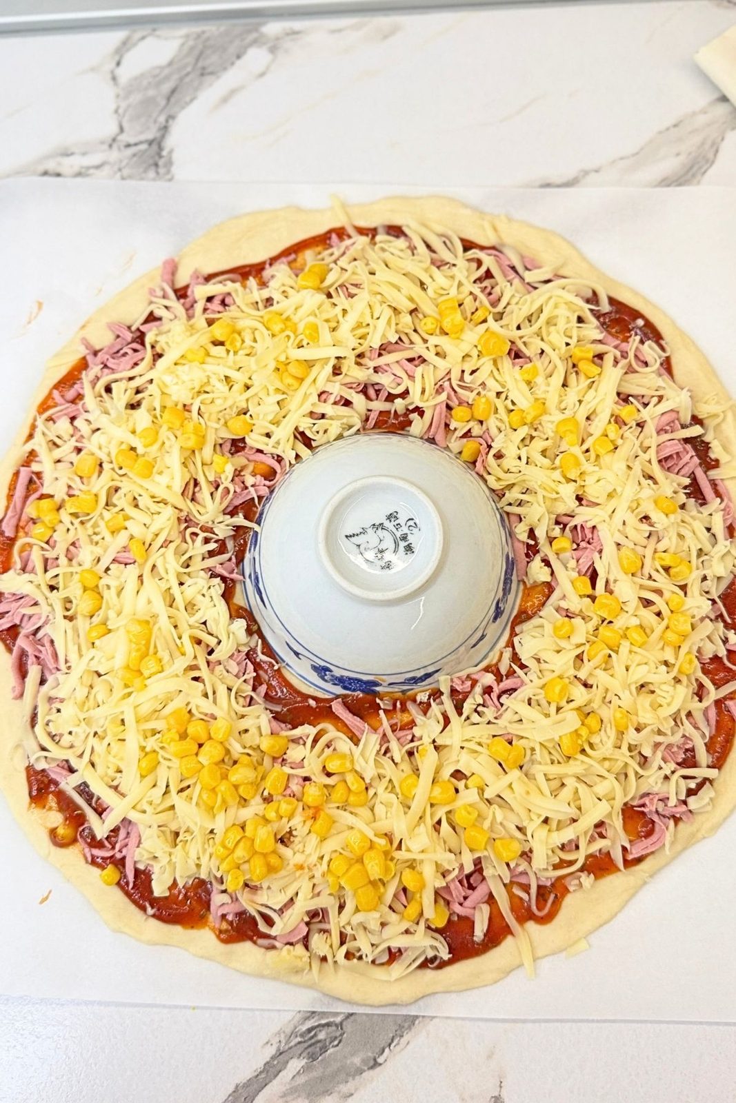 Pizza ring dough topped with tomato sauce, ham, shredded cheese, and corn