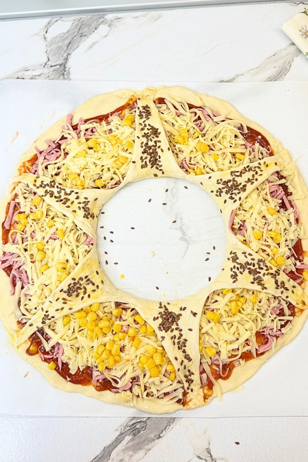 Unbaked pizza ring with folded dough points brushed with water and sprinkled with seeds