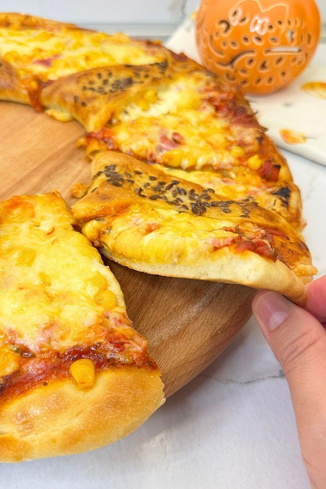 Slice being pulled from a homemade pizza ring with melted cheese, ham, and corn