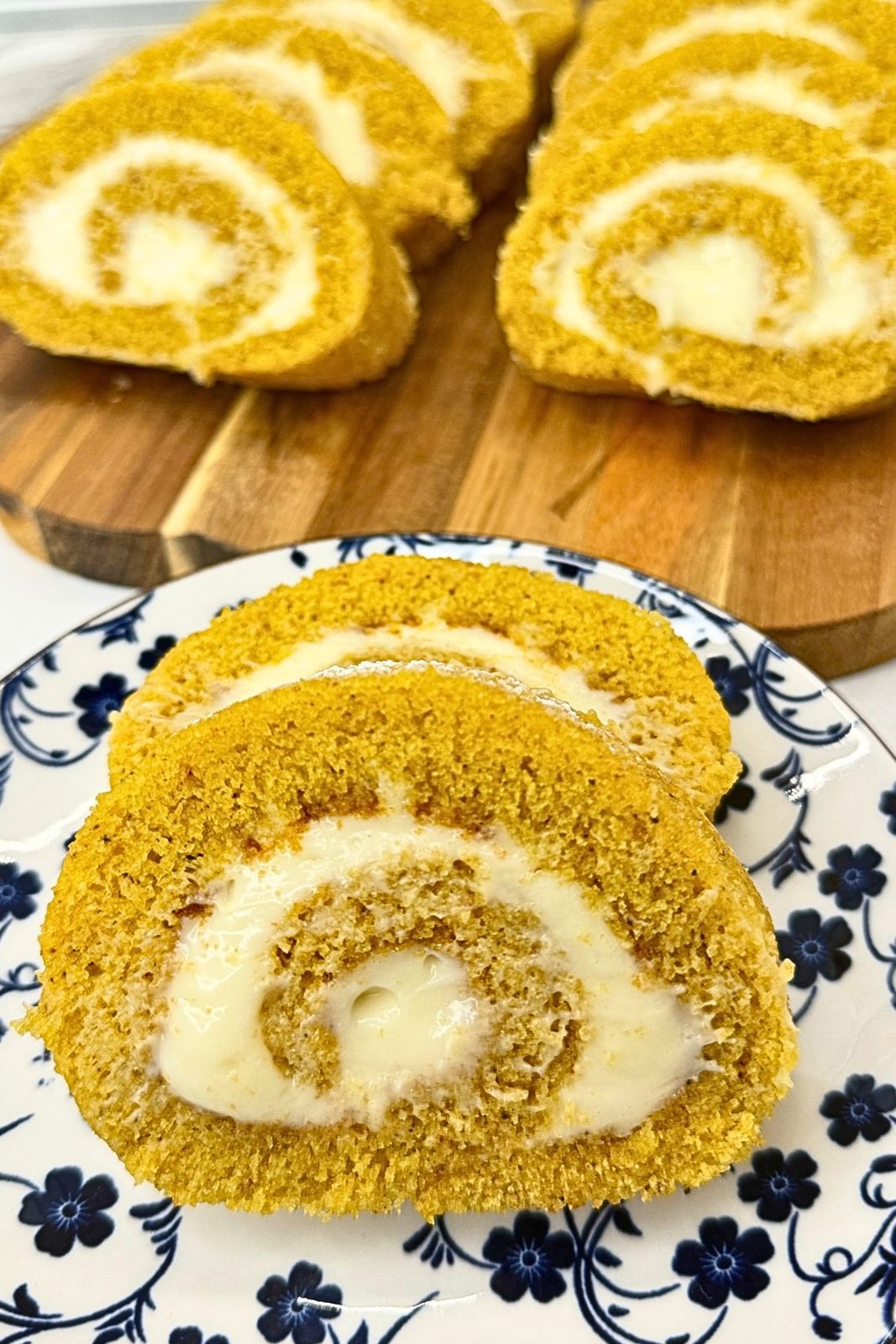 Pumpkin cake roll slices with cream cheese filling on a blue and white floral plate.