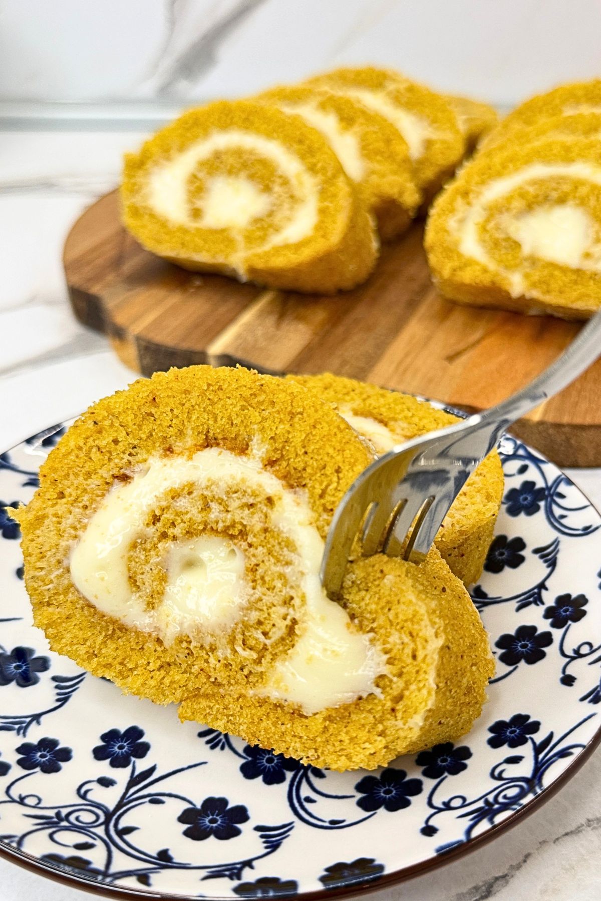 Pumpkin cake roll slices with cream cheese filling on a beige platter with fall decorations.