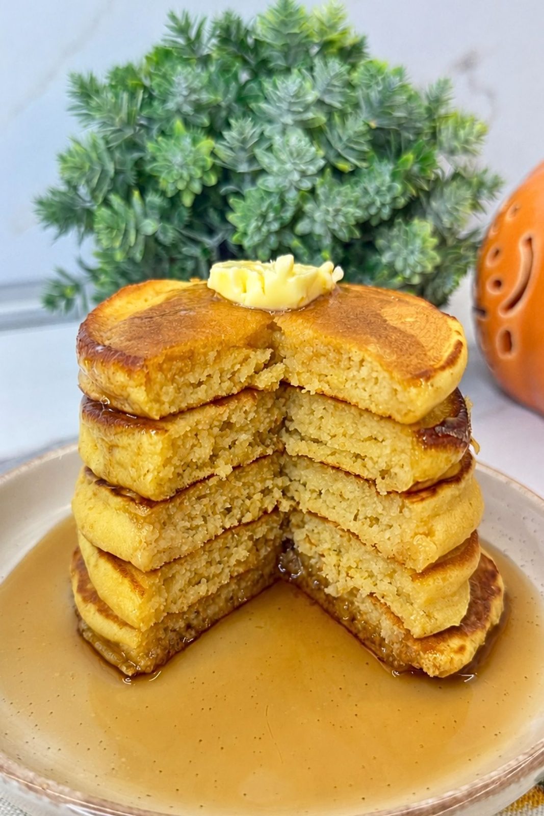 Stack of pumpkin pancakes with a wedge cut out to reveal the soft interior, topped with butter and maple syrup.