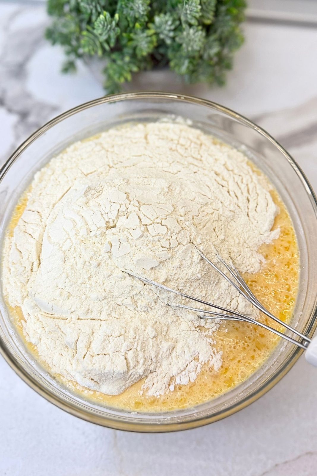 Dry ingredients added to the wet pumpkin pancake mixture in a glass bowl with a whisk.