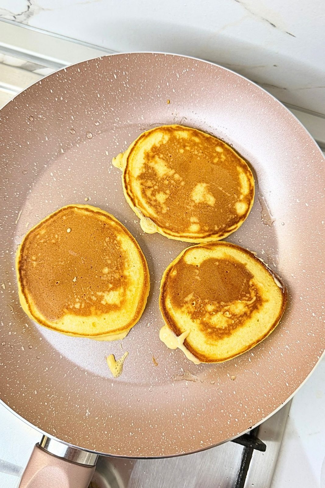 Three golden pumpkin pancakes cooking on the second side in a nonstick skillet.