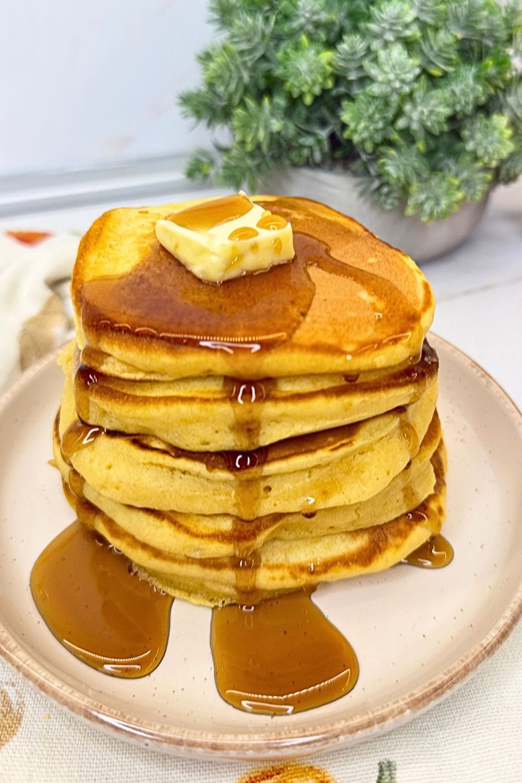 Stack of golden pumpkin pancakes topped with butter and maple syrup on a ceramic plate.