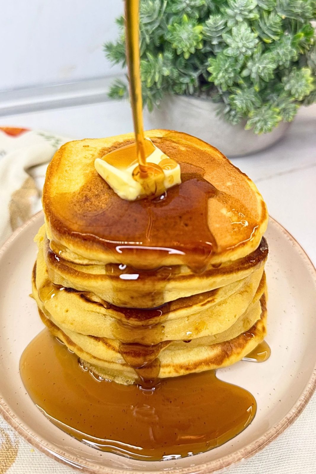Maple syrup being poured over a stack of pumpkin pancakes topped with butter.