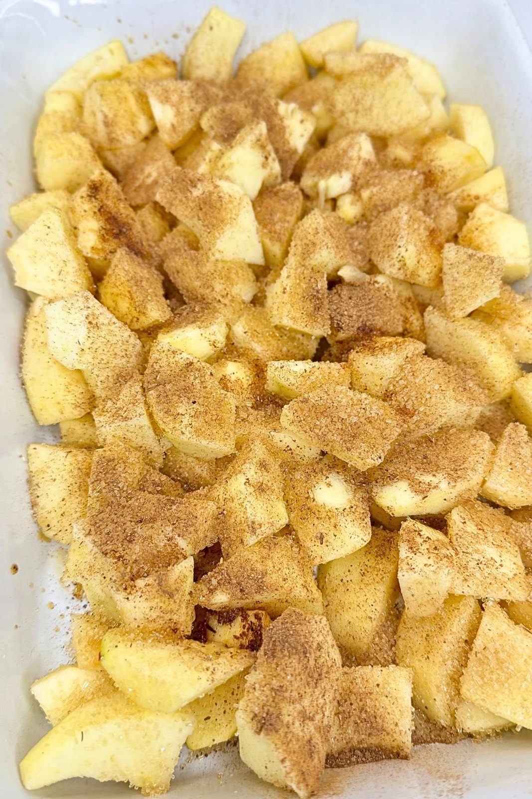 Chopped apples sprinkled with cinnamon and sugar in a white baking dish for homemade apple crisp.