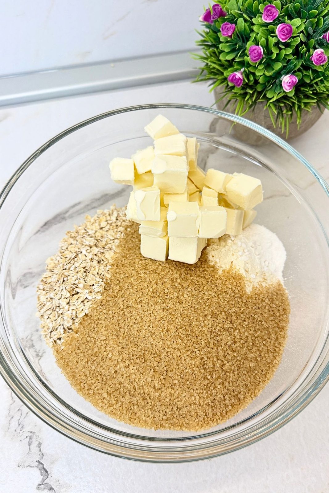 Oats, flour, brown sugar, and cold cubed butter in a glass bowl for apple crisp topping.