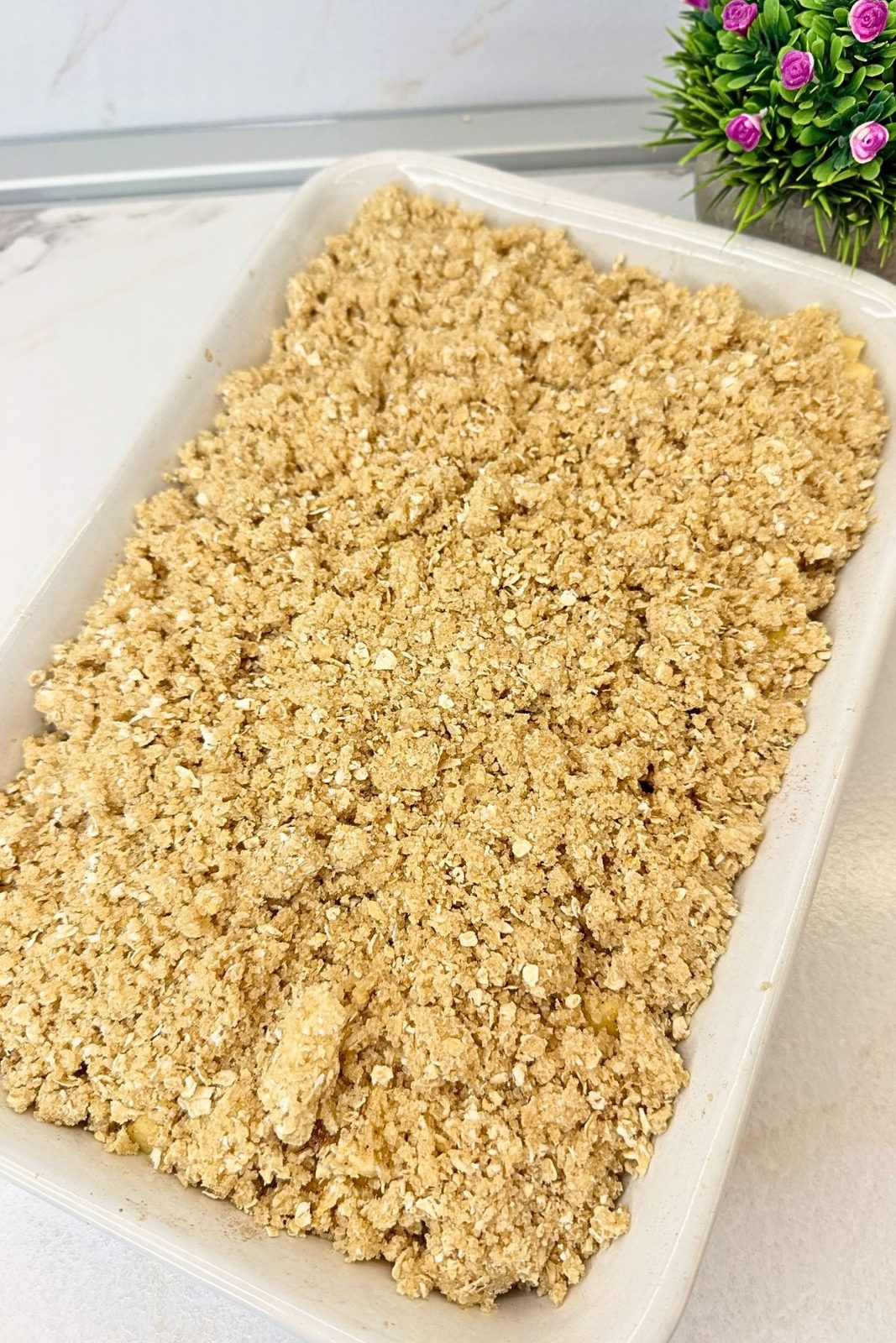 Unbaked apple crisp with an even layer of buttery oat topping covering the apples in a white baking dish.