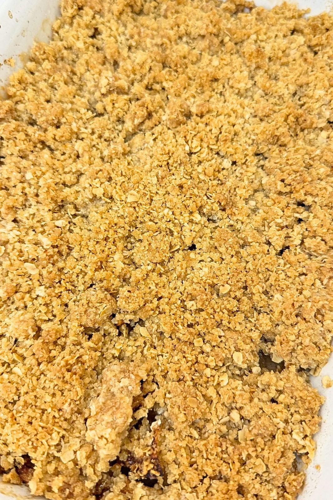 Close-up of baked apple crisp with a golden, buttery oat topping in a white baking dish.