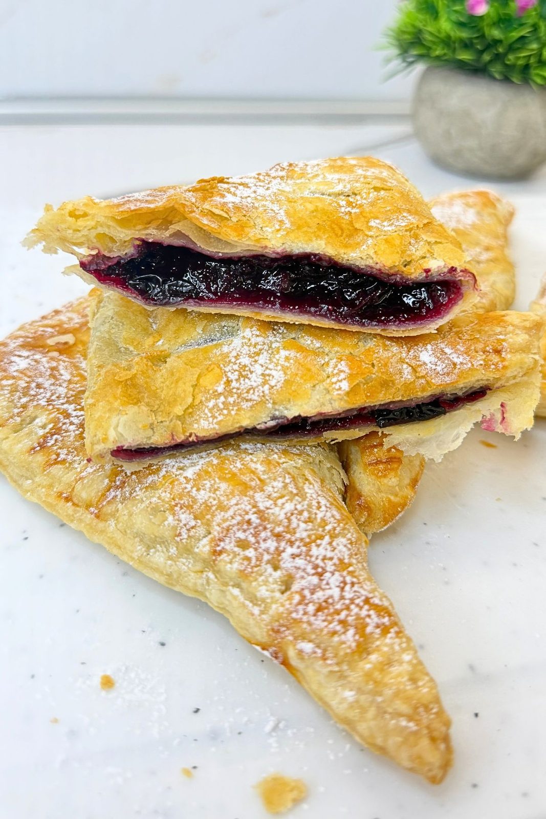 Blueberry turnovers dusted with powdered sugar, with two cut halves stacked on top showing the blueberry filling and flaky pastry layers.
