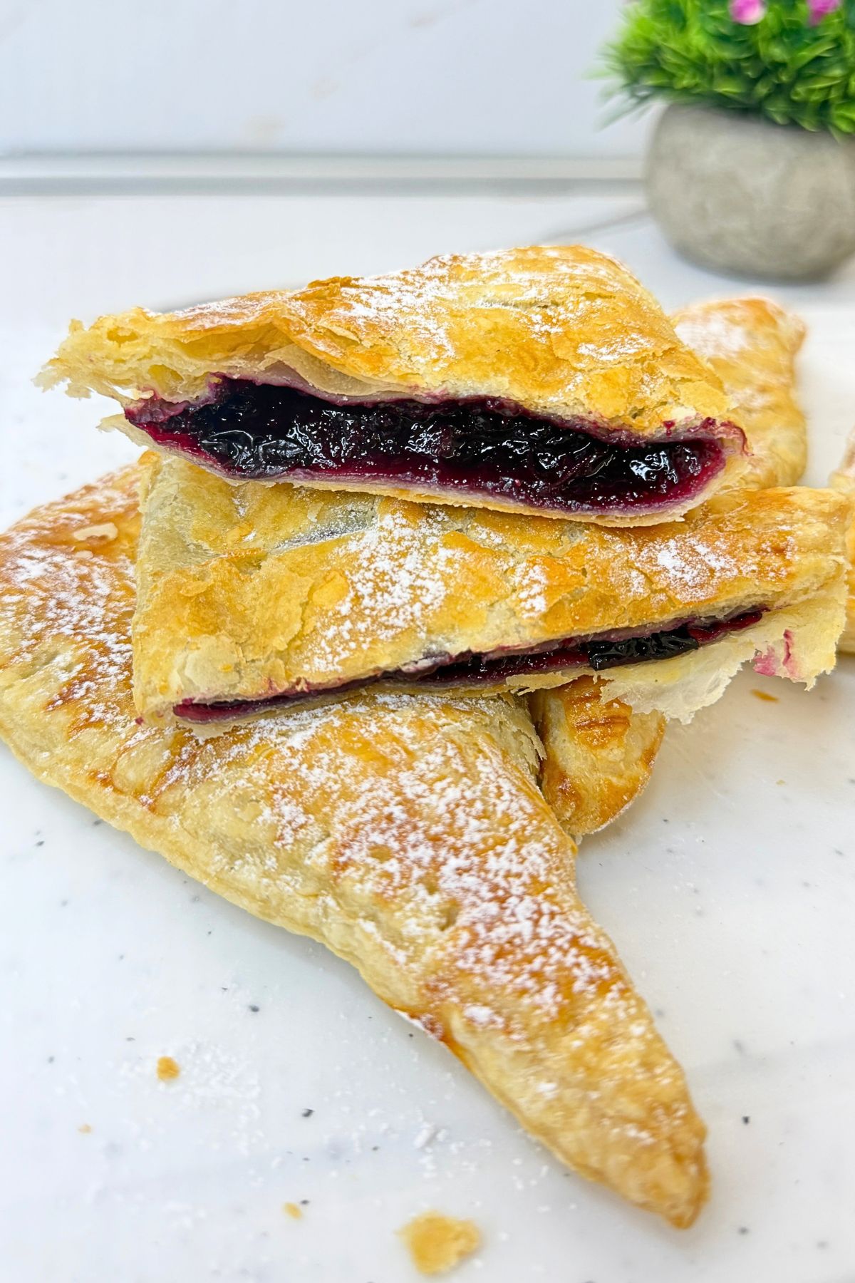 Golden blueberry turnovers dusted with powdered sugar, with cut halves showing the blueberry filling and flaky puff pastry layers.