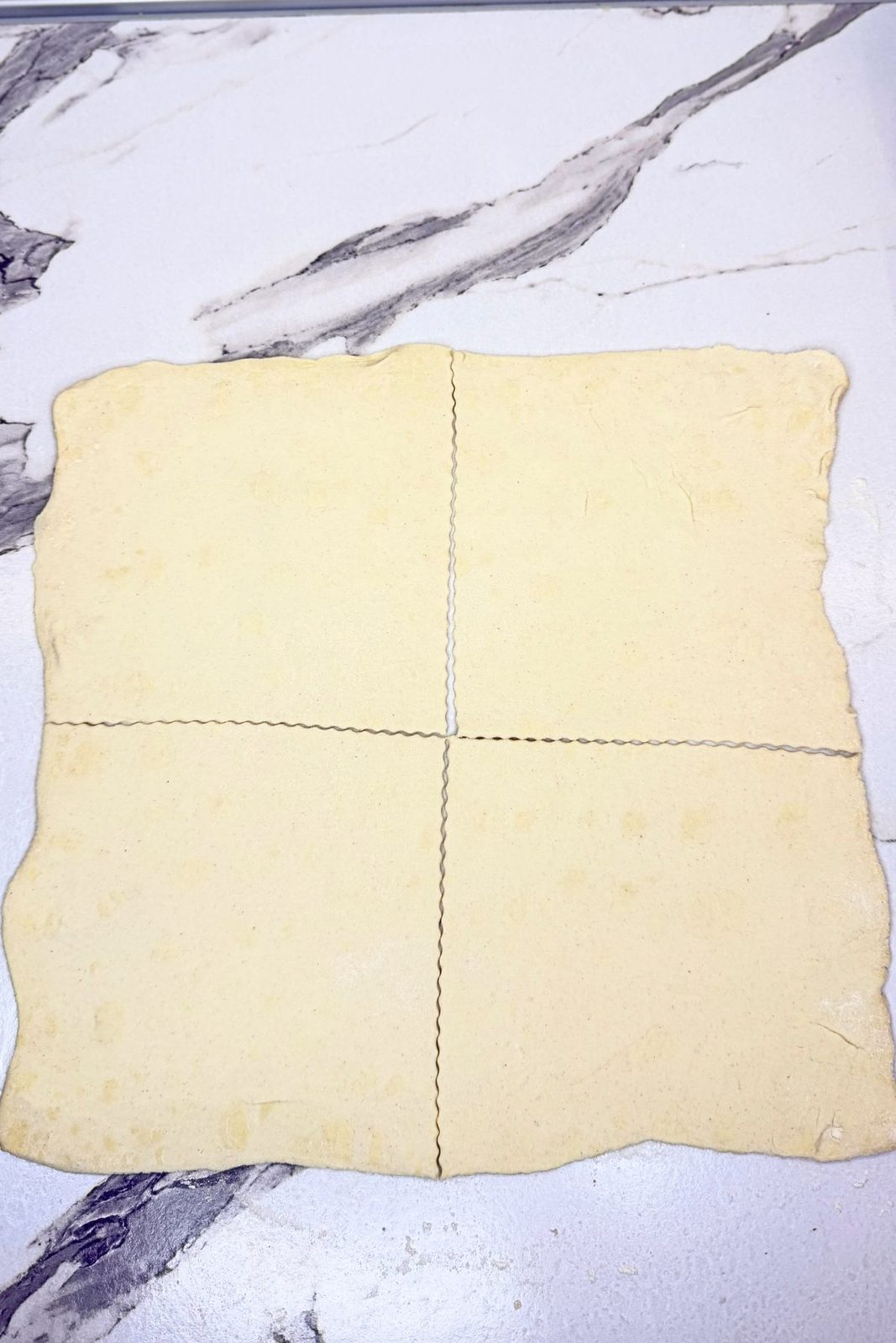 Puff pastry rolled into a square and cut into four equal pieces on a marble countertop.