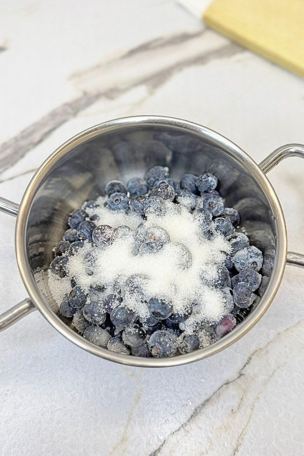 Blueberries and sugar in a saucepan before cooking the blueberry turnover filling.
