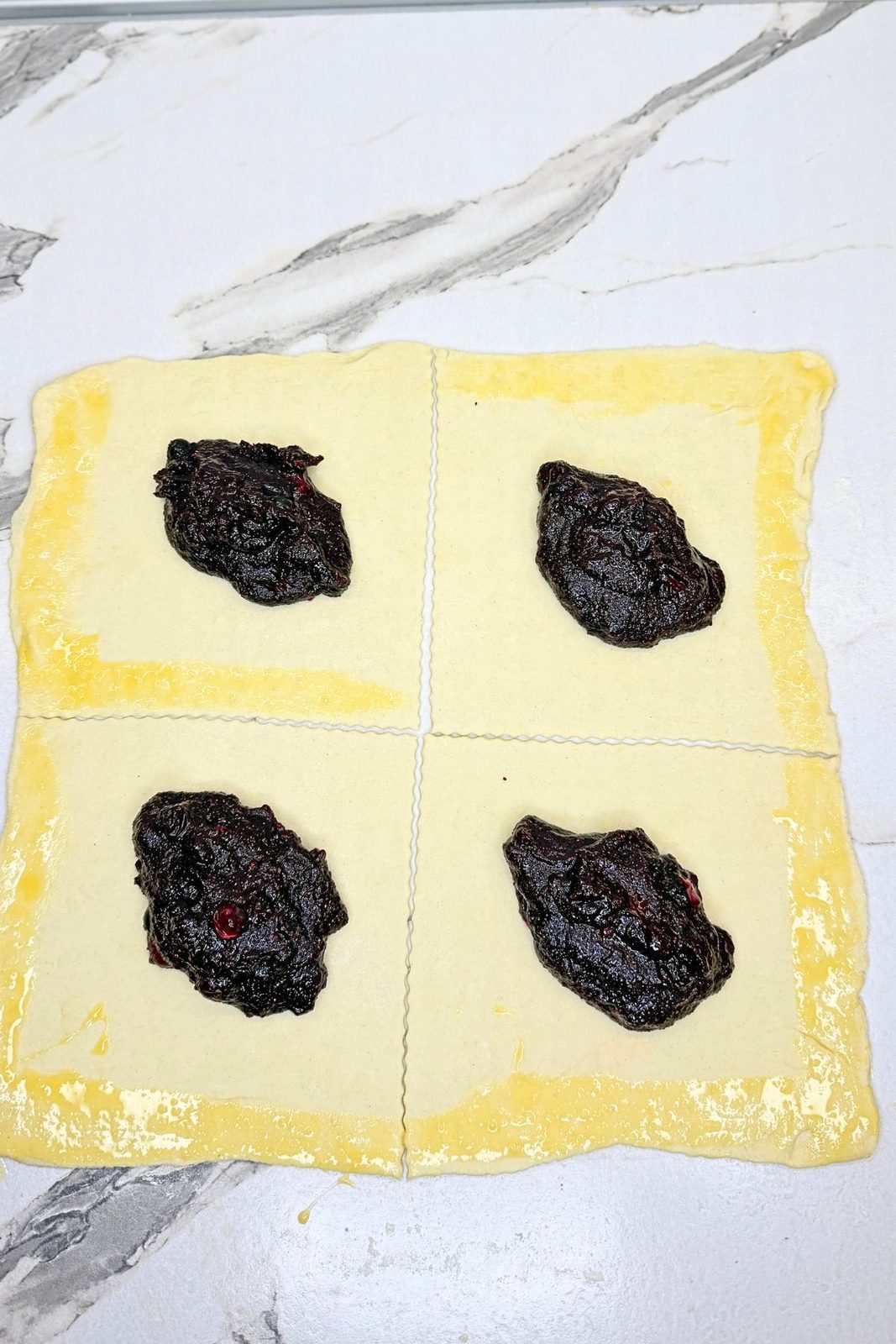 Four puff pastry squares topped with blueberry filling, with egg wash brushed along the edges.