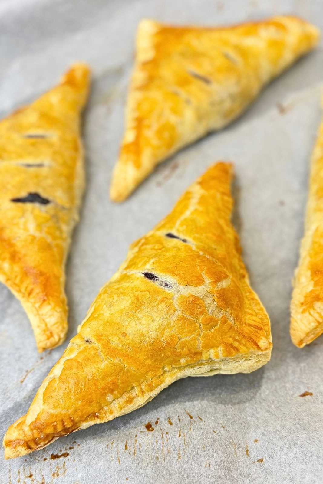 Freshly baked blueberry turnovers with golden puff pastry and crisp edges on parchment paper.