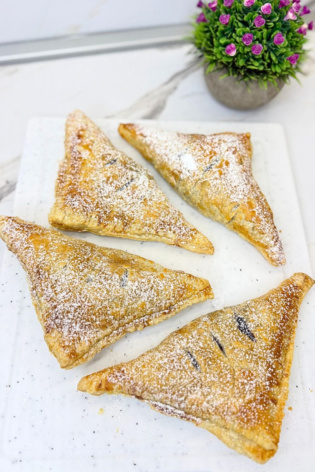Four golden blueberry turnovers dusted with powdered sugar on a white serving board.