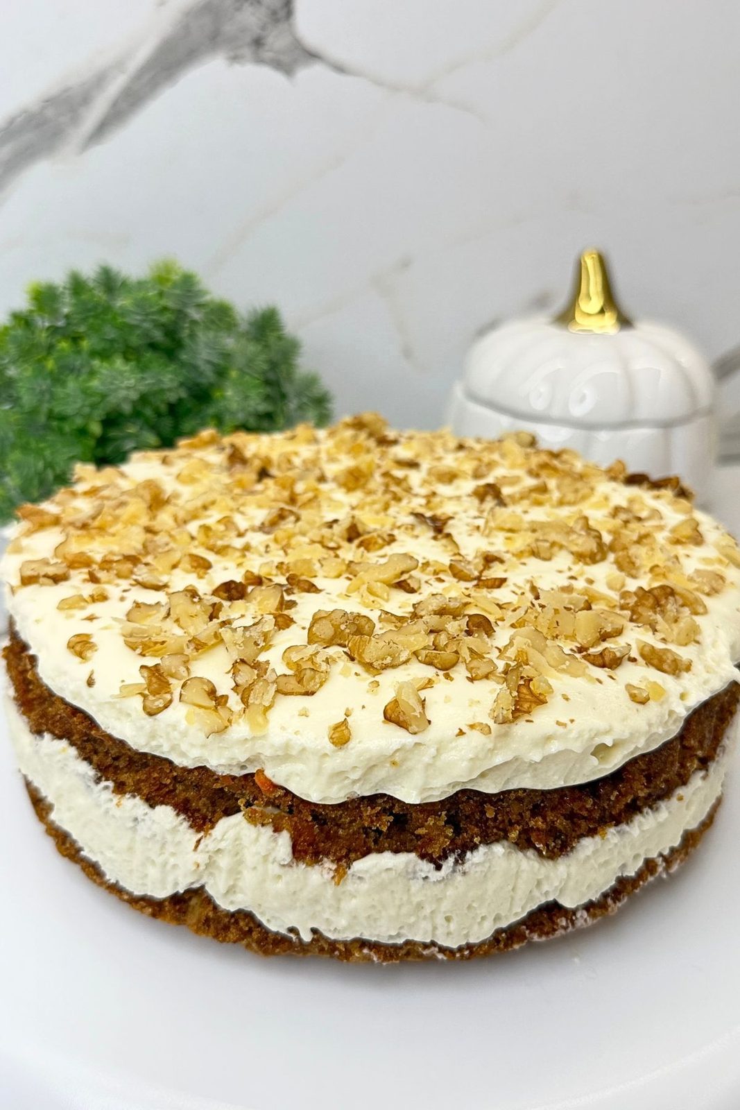 Carrot cake topped with cream cheese frosting and chopped walnuts after chilling.
