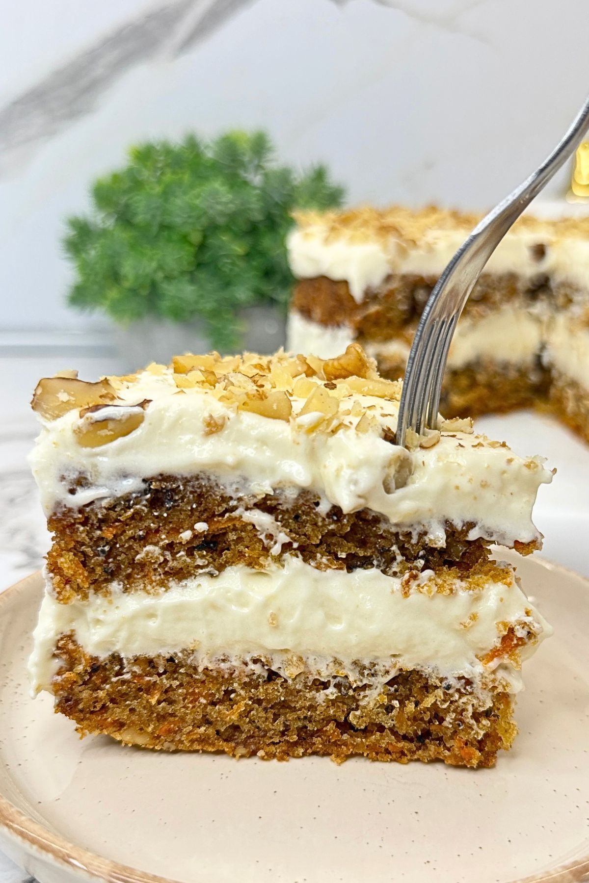 Carrot cake with cream cheese frosting and chopped walnuts, with a slice removed to reveal the moist layers.