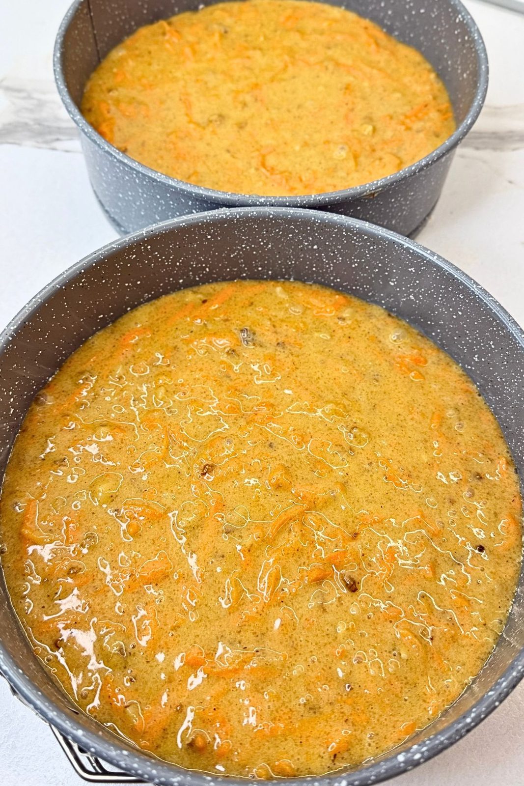 Carrot cake batter divided between two round cake pans lined with parchment paper.