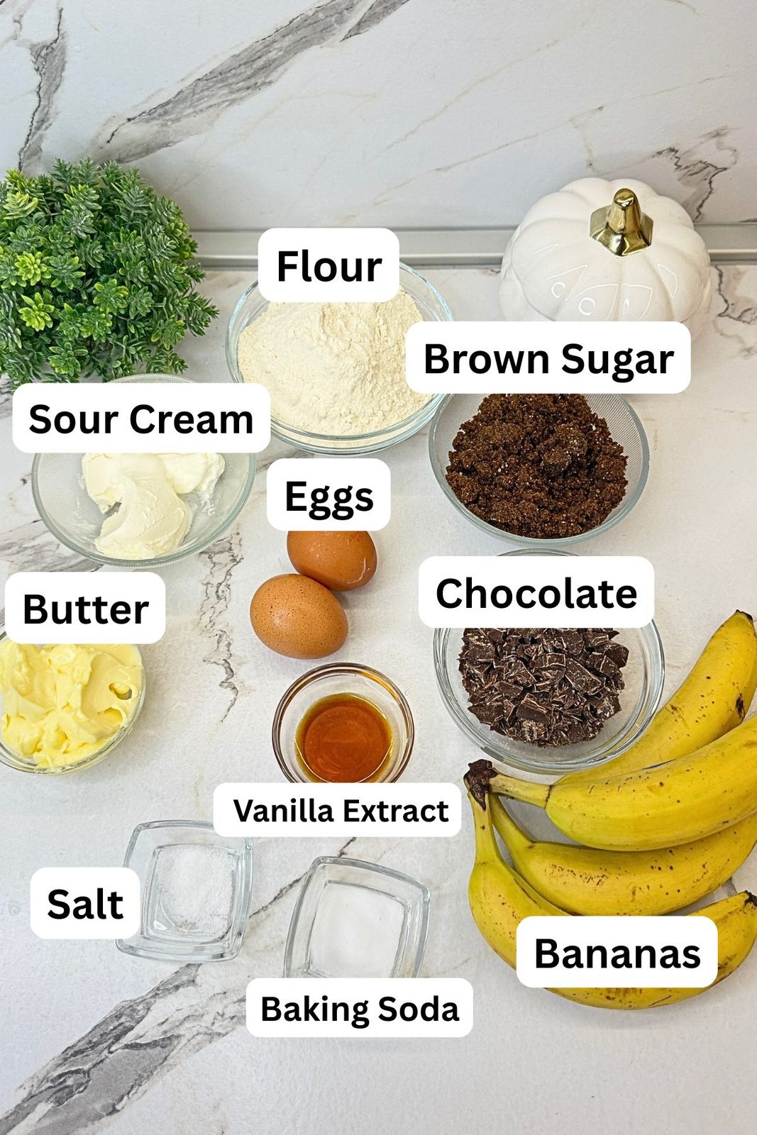 Ingredients for chocolate chip banana bread: flour, brown sugar, butter, eggs, ripe bananas, sour cream, chopped chocolate, vanilla extract, salt, and baking soda.