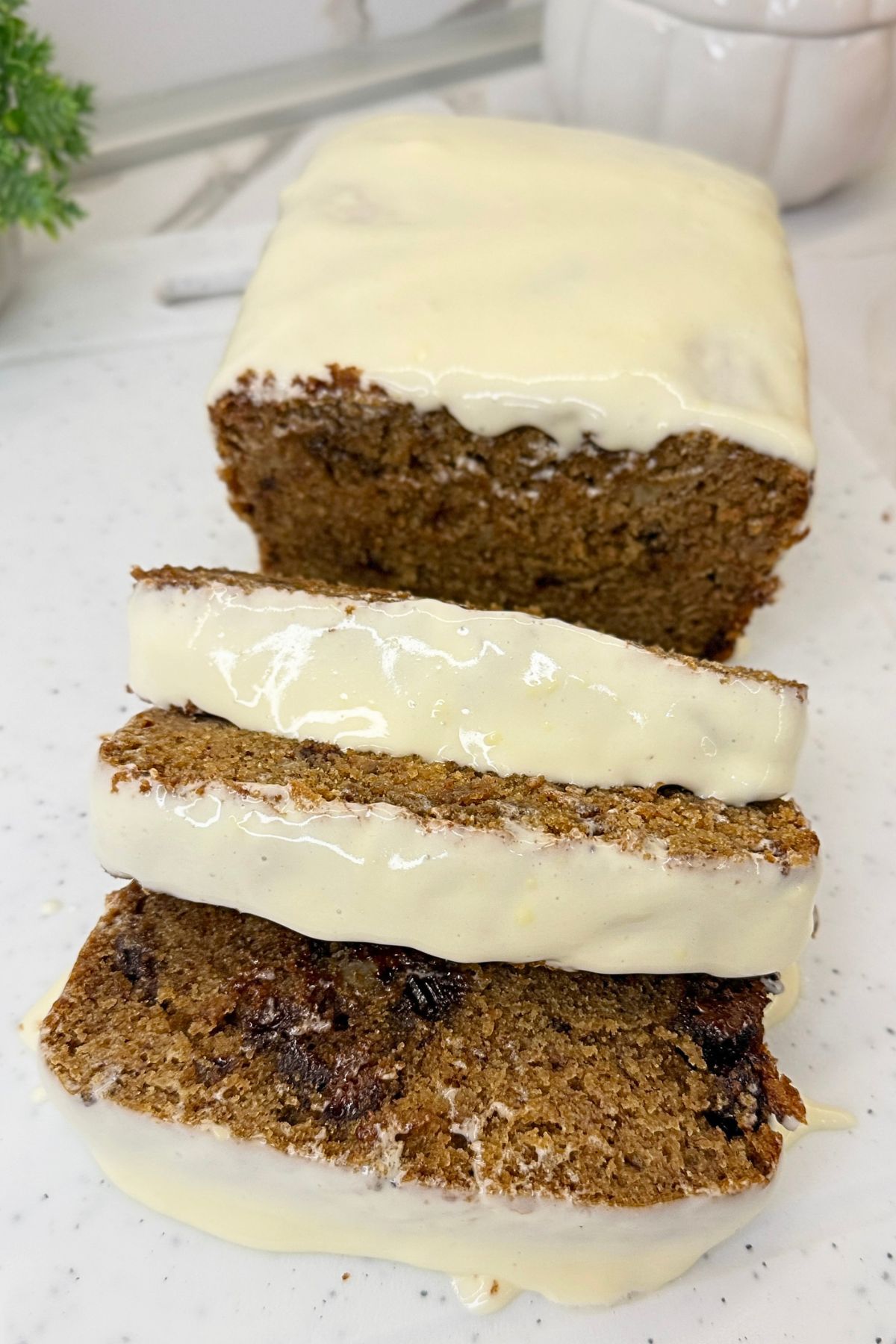 Chocolate chip banana bread topped with cream cheese frosting, sliced to show the moist crumb and chocolate pieces.